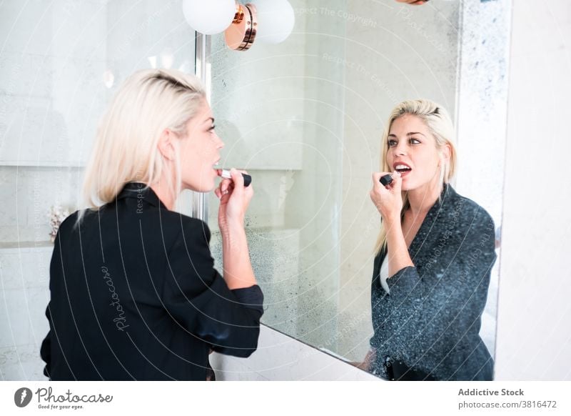 Blonde Frau Anwendung Lippenstift in der Nähe von Spiegel Make-up bewerben Morgen Routine Reflexion & Spiegelung Kosmetik Schönheit jung Farbe Bad Hautpflege