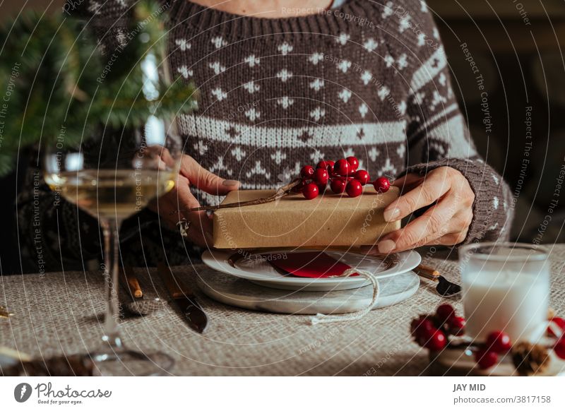 Frau öffnet Weihnachtsgeschenk, während sie am gedeckten Tisch sitzt, Family Together-Konzept Weihnachten offen Geschenk Weihnachtstisch decken Glück Menschen