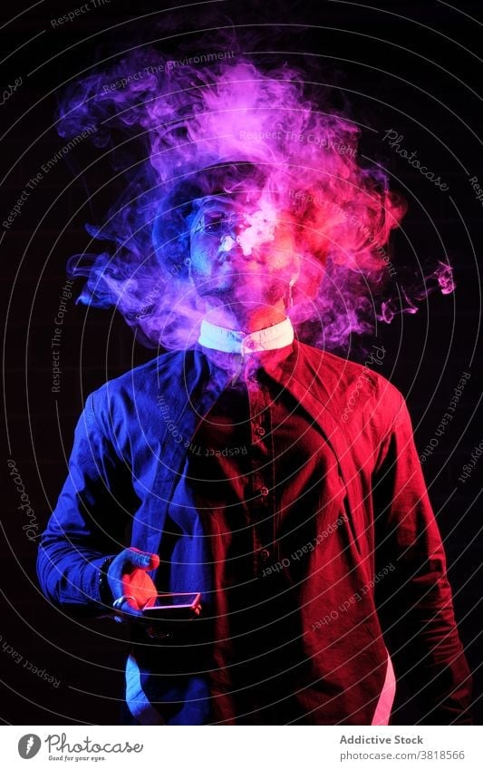 Schwarzer Mann rauchend im Studio mit Neon-Beleuchtung neonfarbig Licht Rauch Raps Dampf Verdunstung Stil Outfit selbstbewusst männlich ethnisch schwarz