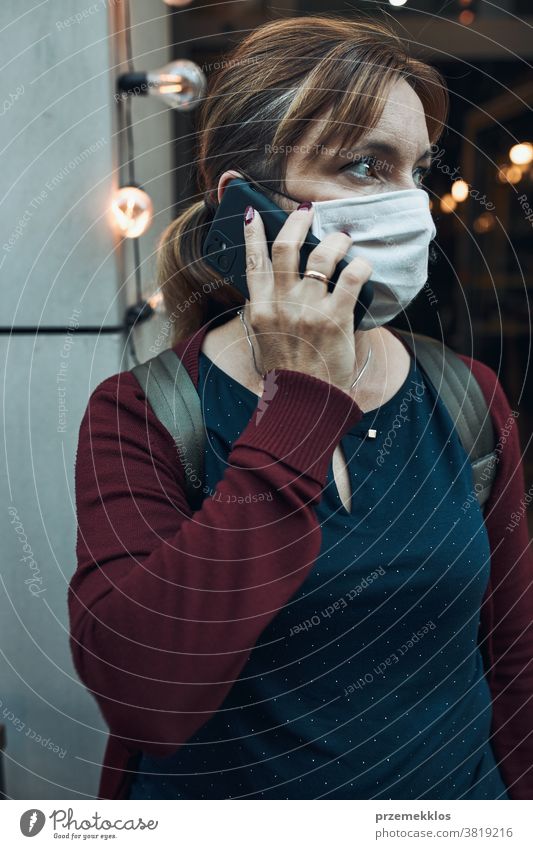 Junge Frau, die vor einem Restaurant in der Innenstadt telefoniert und die Gesichtsmaske trägt, um eine Virusinfektion zu vermeiden Anruf Pflege Kaukasier