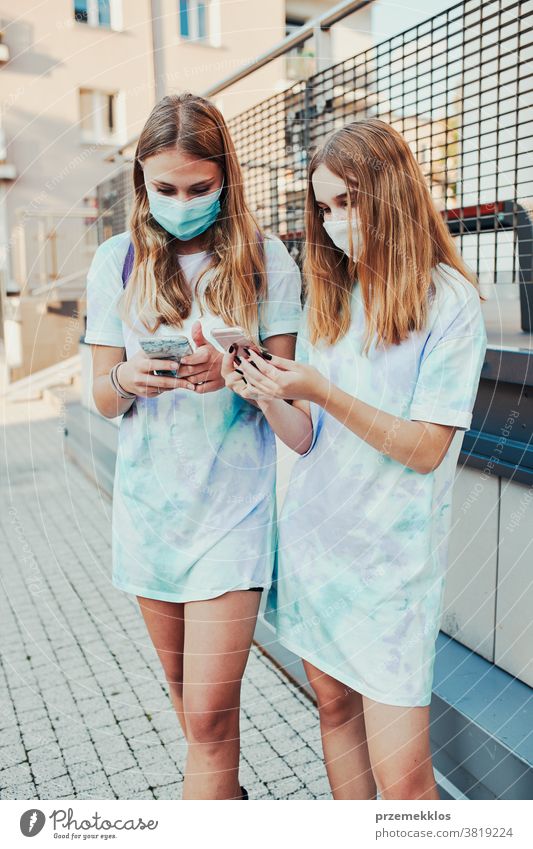 Junge Frauen, die Smartphones benutzen und die Gesichtsmasken tragen, um eine Virusinfektion zu vermeiden, wenn sie auf der Straße stehen Kaukasier Funktelefon