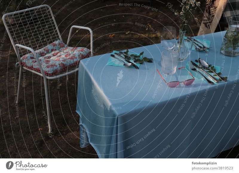 gedeckter Gartentisch mit blauer Tischdecke, Gartenstuhl, Blumenkissen und Sonnenbrille Gartenleben Gartenmöbel Sommerfest gedeckter Tisch gemeinsam Laube
