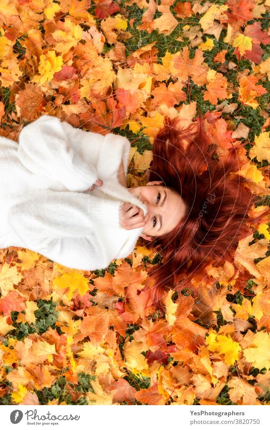 Schöne rothaarige Frau auf Herbstlaub liegend. Junge Frau lächelt in Herbstlandschaft 20s November Oktober obere Ansicht Erwachsener allein Herbstmode