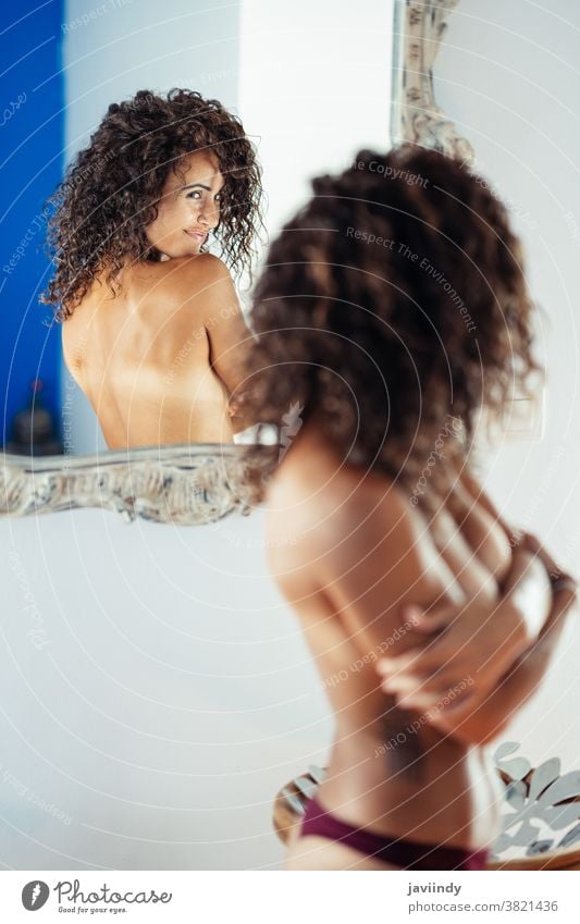 Frau mittleren Alters in Oben-ohne, die sich selbst in einem Wandspiegel betrachtet. oben ohne 40s Dessous Spiegel Schönheit Mädchen Boudoir Mode erotisch