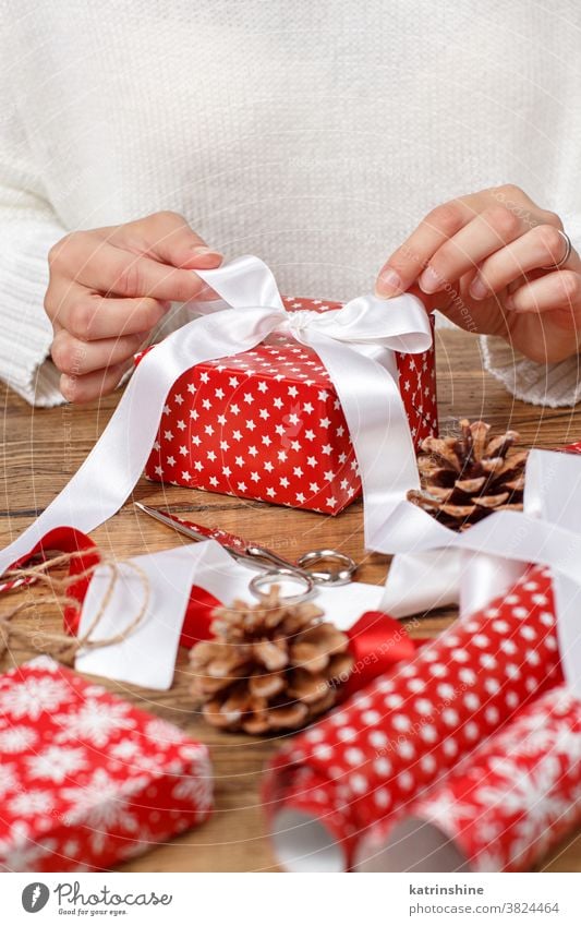 Frau bindet eine Bandschleife an ein verpacktes Geschenk Hände Krawatte Schleife Bändchen abschließen Geschenkverpackung präsentieren Weihnachten Pullover rot