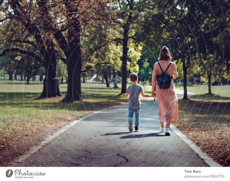 Hand in Hand Mutter mit Kind spaziert durch einen herbstlichen Park Stadt Spaziergang Spazierweg spazieren spazierengehen Mutter mit Sohn Junge Frau Liebe