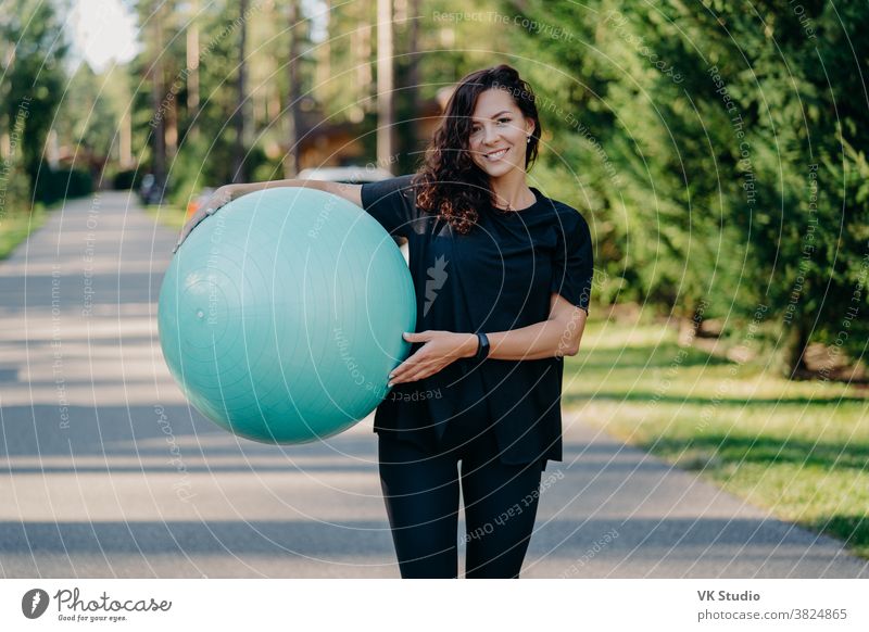 Außenaufnahme einer brünetten Frau posiert mit einem großen Fitball, in Sportkleidung gekleidet, trainiert unter freiem Himmel, geht auf der Straße, posiert in Waldnähe. Fitnesstrainerin geht in die Meisterklasse für schwangere Frauen
