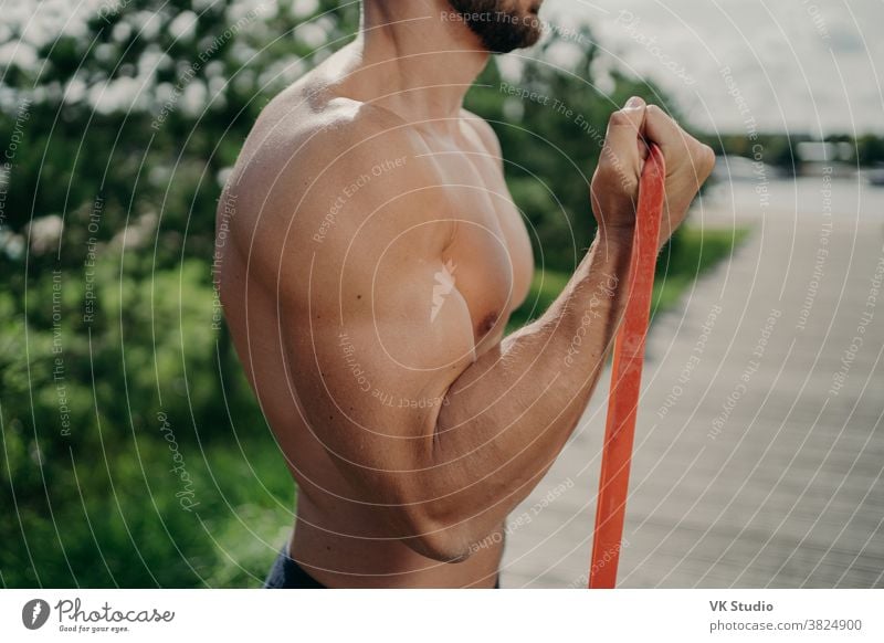 Cropped shot eines nicht erkennbaren muskulösen Mannes hat Training Bizeps Übung steht im Profil zeigt starke Muskeln, verwendet Widerstandsband, strebt nach starkem Körper. Bodybuilding, Motivationskonzept