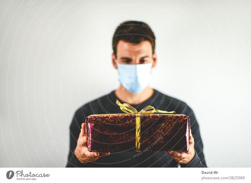 Corona und Weihachten - Mann mit Maske hält Geschenk in den Händen Weihnachten Atemschutzmaske Mundschutz abstand Pandemie schenken