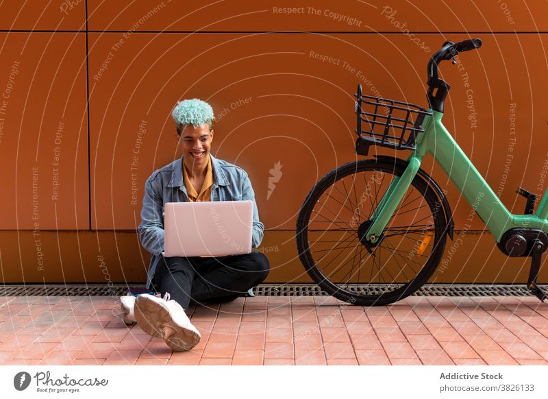 Ethnischer informeller männlicher Freiberufler, der in der Stadt arbeitet freiberuflich Hipster Mann abgelegen Arbeit sprechen benutzend Laptop blaue Haare