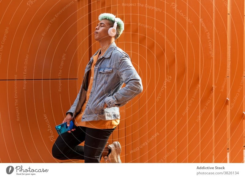 Verträumter ethnischer Mann beim Musikhören in der Stadt Kopfhörer Großstadt zuhören verträumt Hipster blaue Haare informell Gesang männlich schwarz