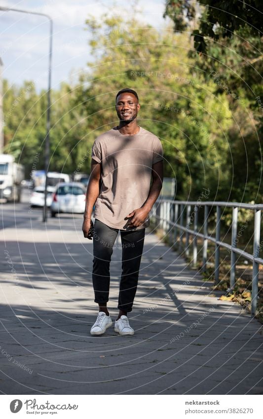 Junger schwarzer Mann geht auf dem Bürgersteig der Stadt Lächeln afrikanische ethnische Zugehörigkeit Spaziergang Straße echte Aufrichtigkeit reales Leben