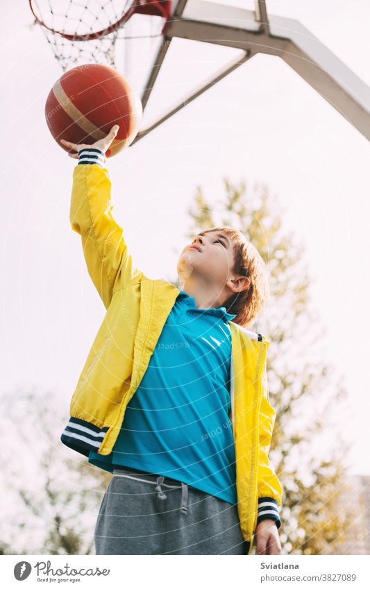 Porträt eines süßen Basketball-Spielers, der mit einem Ball in der Hand neben dem Basketballkorb steht. Das Konzept des Sports und eines gesunden Lebensstils