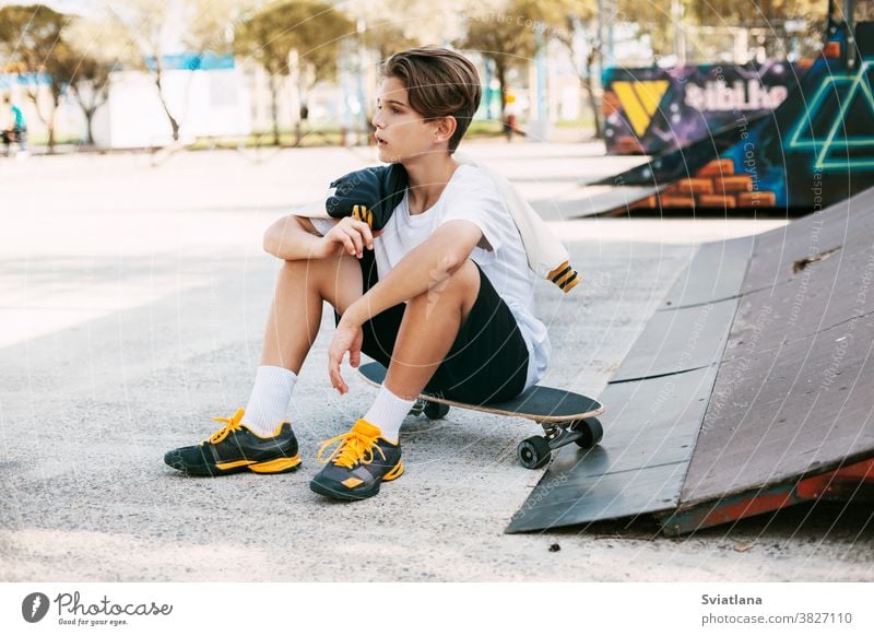 Ein wunderschöner Teenager sitzt auf einem Skateboard in einem speziellen Bereich des Parks. Ein Junge ruht sich nach einer Fahrt in einem Skatepark aus. Aktive Erholung an der frischen Luft