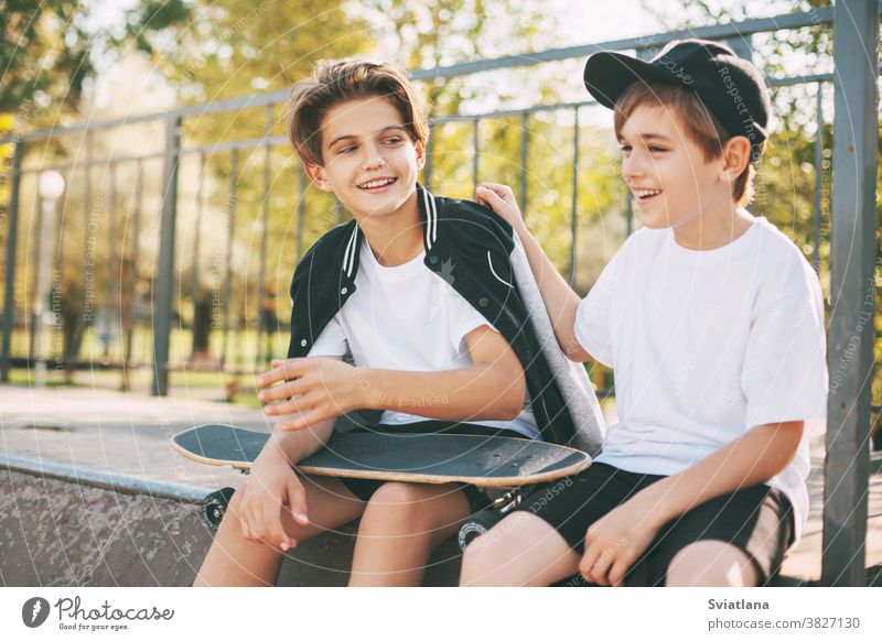 Zwei süße Teenager sitzen in einem Skatepark, entspannen sich nach dem Skateboarden und unterhalten sich. Die Jungs genießen ihre Freizeit im Skatepark, auf der Rampe sitzend. Das Konzept von Jugend, Einheit und Freundschaft