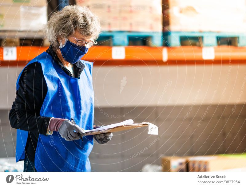 Ältere weibliche Lagerarbeiter schreiben in Zwischenablage in der Nähe von Regalen Frau Arbeiter Aufzeichnen Vorgesetzter Kontrolle Papierkram