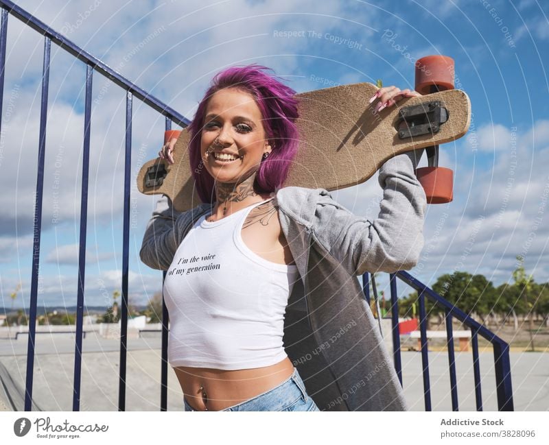 Entschlossene Frau mit Longboard in der Stadt tausendjährig unabhängig informell jung rosa Haare ausgefallen Skater selbstbewusst modern Hipster Mode trendy