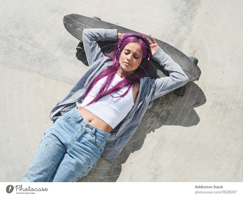 Entschlossene Frau mit Longboard in der Stadt tausendjährig unabhängig informell jung rosa Haare ausgefallen Skater selbstbewusst modern Hipster Mode trendy