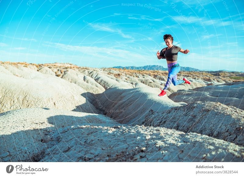 Energetische Sportlerin beim Laufen in der Wüste auf hügeligem Terrain laufen springen wüst rau Ödland aktiv felsig Energie Athlet Frau Berghang Gelände Natur