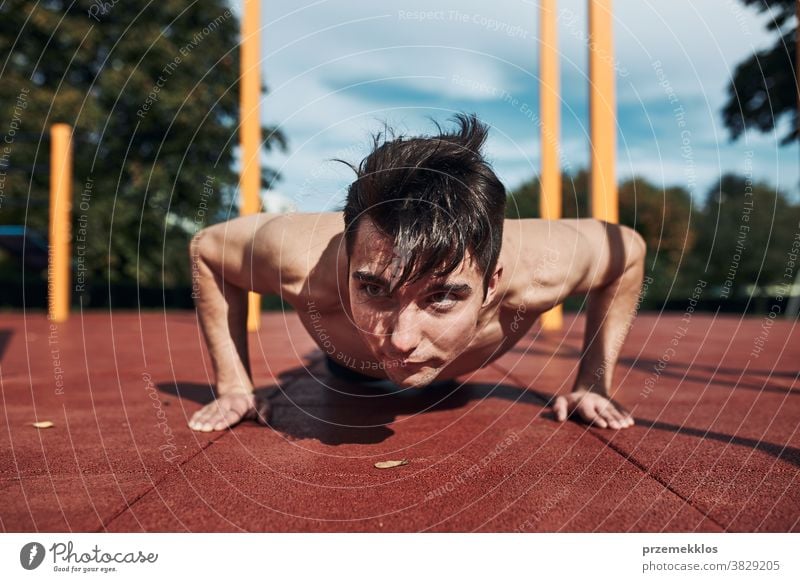Junger hemdloser Bodybuilder macht Liegestützen auf rotem Gummiboden während seines Trainings in einem modernen Gymnastikpark calisthenics Pflege Kaukasier