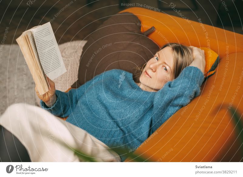 Ein schönes Mädchen entspannt sich auf dem Sofa im Wohnzimmer und liest ihren Lieblingsroman. Ein süßes, nachdenkliches Mädchen liegt auf dem Sofa und liest ein Buch. Online arbeiten, freiberuflich tätig, soziale Distanz