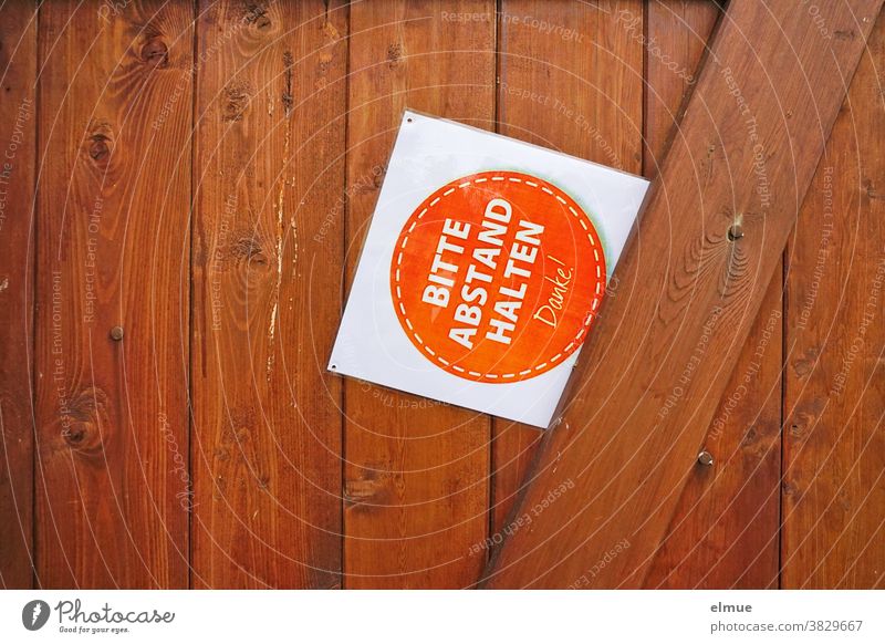 Schild mit der Aufschrift "BITTE ABSTAND HALTEN - Danke!" klemmt schräg an einer braunen Holztür Bitte Abstand halten Sicherheitsabstand schützen klemmen