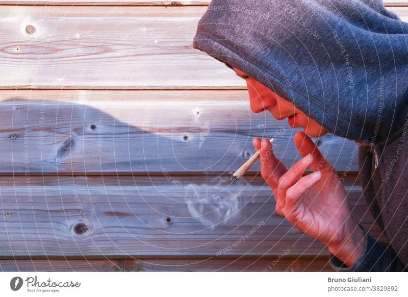 Junge mit einer gedrehten Zigarette mit faltiger Hand. Mann, der allein Marihuana gegen einen hölzernen Lattenzaun raucht. Medikament Gelenk Porträt Cannabis