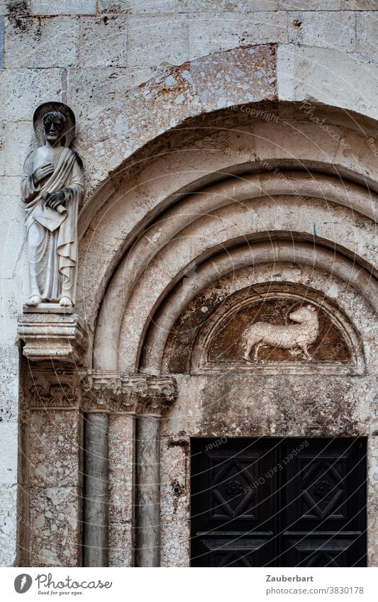 Lamm als Relief und Statue eines Heiligen an einem romanischen Kirchenportal mit Rundbogen Heiliger Portal alt Religion religiös Verehrung Religion & Glaube