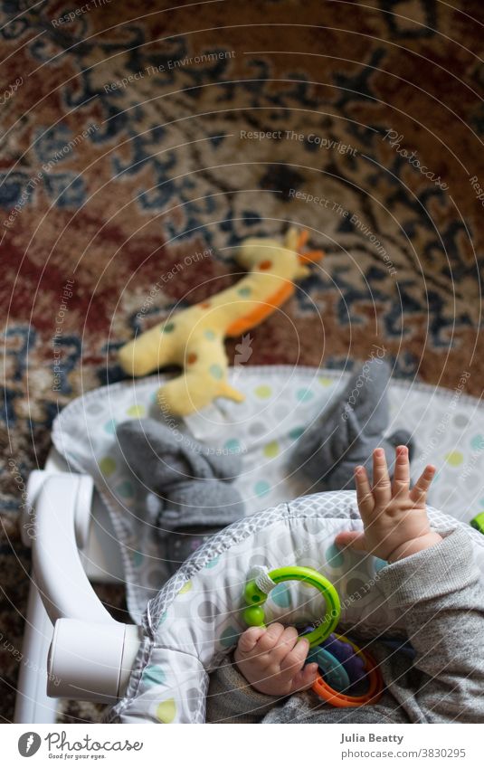 Baby sitzend mit Spielzeug auf orangem Teppich; nach Giraffenspielzeug greifend Säugling Kind 0-12 Monate Kindheit Kunststoffringe Schühchen Tropfen