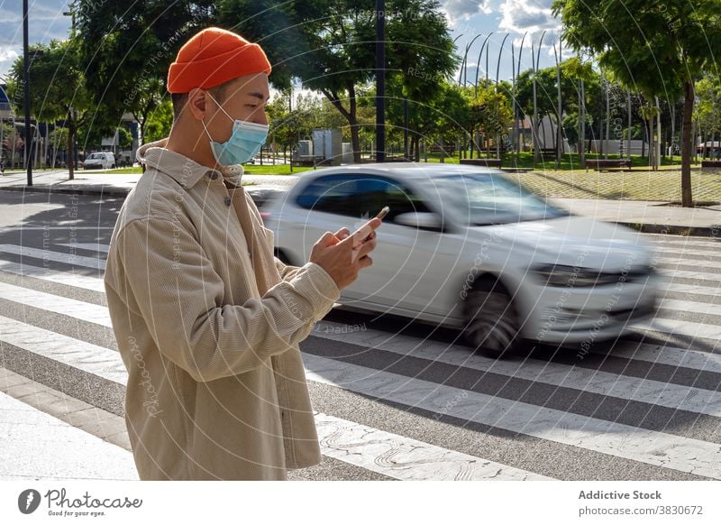 Ruhiger asiatischer Mann, der auf der Straße in der Nähe eines fahrenden Autos auf seinem Smartphone surft benutzend Zebrastreifen Browsen Funktelefon