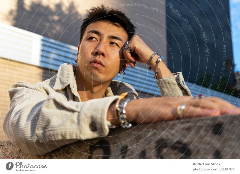Nachdenklicher asiatischer Mann lehnt sich mit der Hand an ein Backsteingebäude nachdenklich besinnlich sich auf die Hand lehnen ruhen Windstille nachdenken