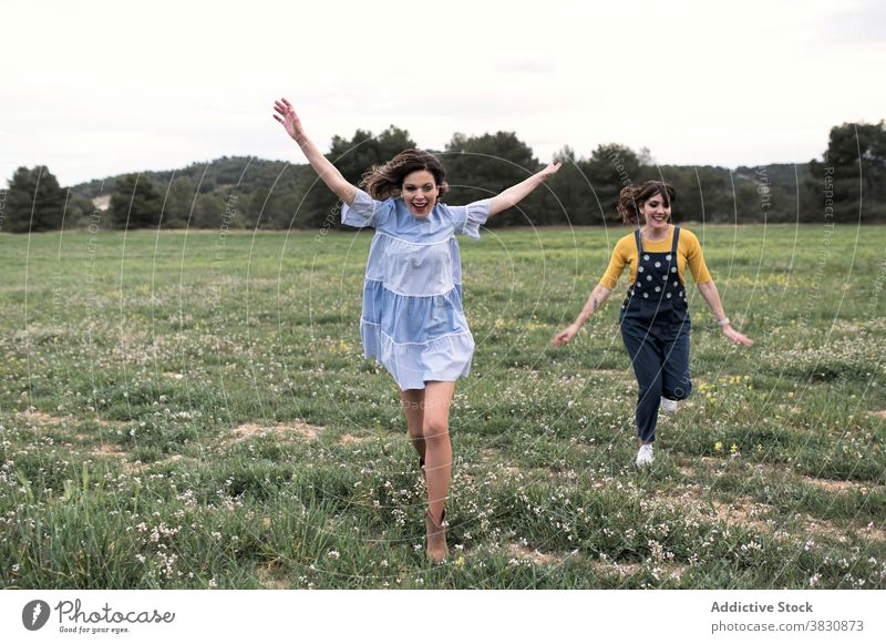 Positive Frauen laufen durch Wiese Glück aufgeregt sorgenfrei Spaß haben Sommerzeit schlanke Natur heiter Zahnfarbenes Lächeln Harmonie Arme hochgezogen Feld
