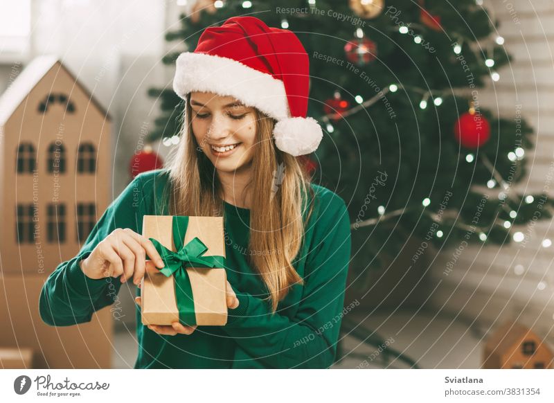 Hübsche Teenagerin öffnet ein Geschenk aus Kraftpapier, das mit einem grünen Band gebunden ist, Neujahrsstimmung. Feiertagskonzept von Weihnachten und Neujahr zu Hause.