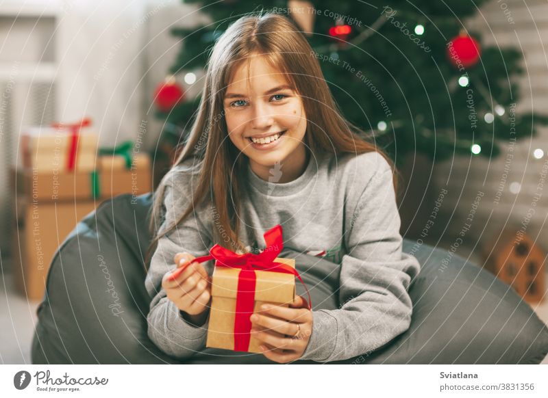 Hübsche Teenagerin öffnet ein Geschenk aus Kraftpapier, das mit einem roten Band gebunden ist, Neujahrsstimmung. Feiertagskonzept von Weihnachten und Neujahr zu Hause.