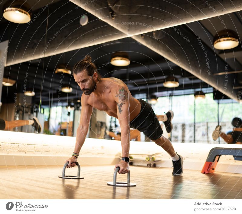 Bärtiger Sportler beim Training an Liegestützgriffen Fitnessstudio hochschieben Handgriff Übung Gleichgewicht modern ohne Hemd männlich Erwachsener Athlet