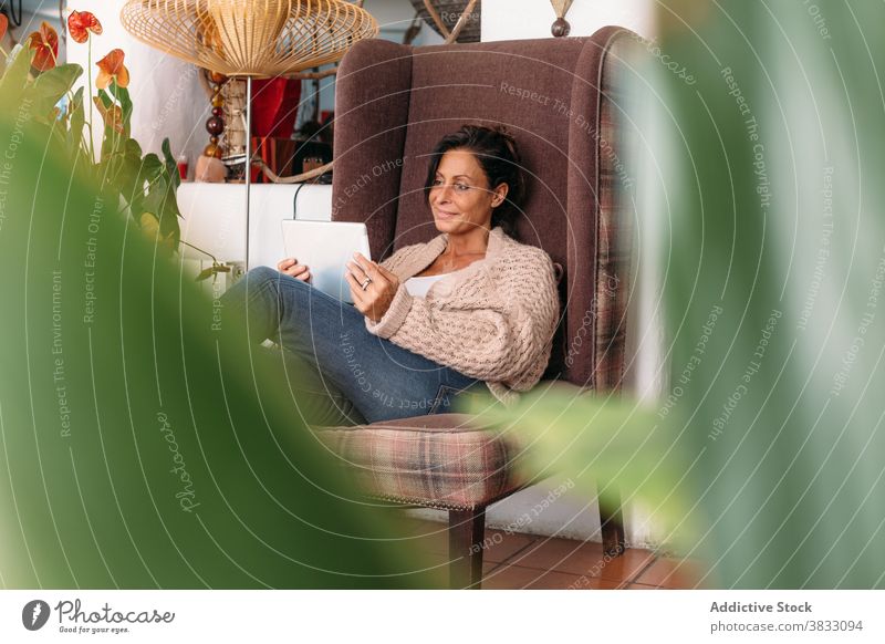 Erwachsene Frau mit Tablette Chillen in gemütlichen Stuhl zu Hause ruhen Kälte lesen benutzend positiv ethnisch Erwachsener Wochenende Komfort