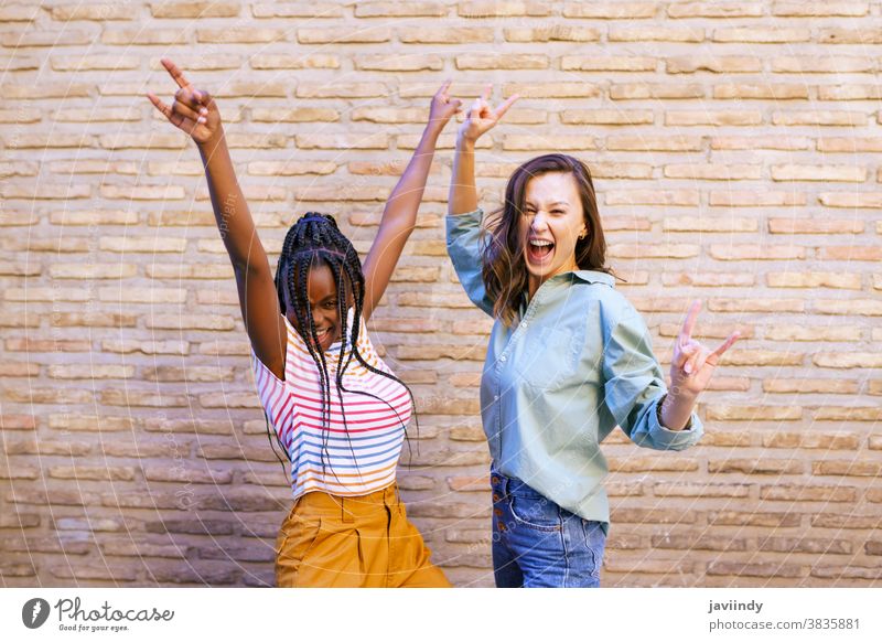 Zwei Freundinnen amüsieren sich gemeinsam auf der Straße. Multiethnische Freunde. Frauen multiethnisch Zeichen Hupe Zopf Frisur Behaarung schwarz Afro-Look