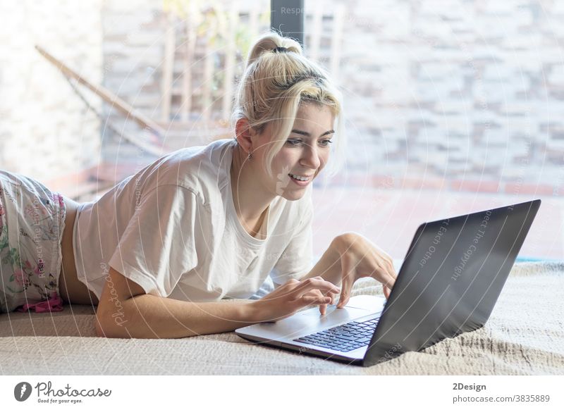 Lächelnde Frau, die einen Laptop benutzt, während sie auf ihrem Bett liegt Person Teenager Cyberspace Fröhlichkeit Erholung Computer Glück heimwärts