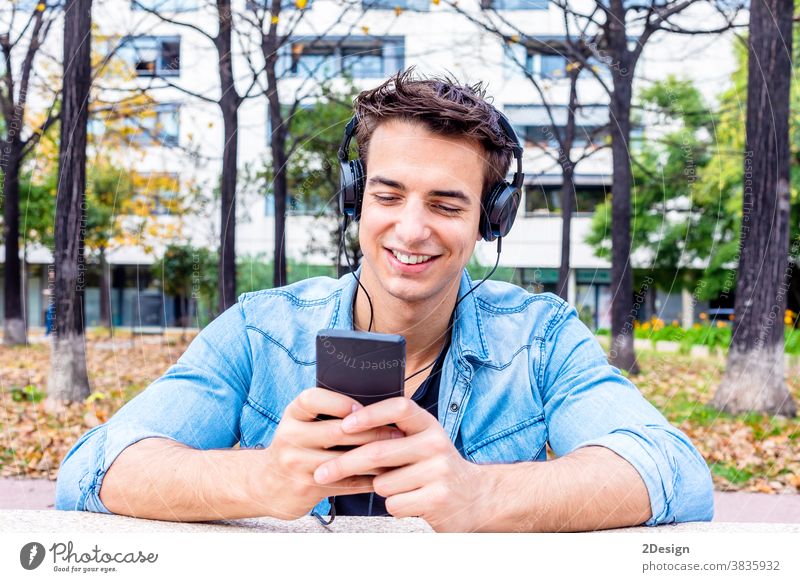 Junger Mann sieht Smartphone mit Kopfhörer auf dem Kopf Sitzen Glück hören Lächeln jung Mobile Typ Technik & Technologie Person Musik Handy benutzend urban