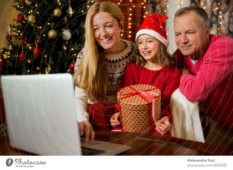 Ein glückliches Paar mit einem Kind feiert Weihnachten mit seinen Freunden per Videoanruf per Webcam. Die Familie begrüßt ihre Verwandten am Heiligabend online. Neu normal