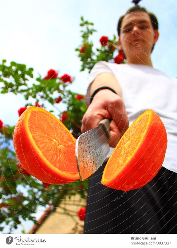 Ein Mann und eine Orange, von einem Küchenmesser in zwei Hälften geschnitten. Eine Frucht voller Vitamine. Vegetarisches oder veganes Essen. Absichtlich verschwommener Hintergrund.