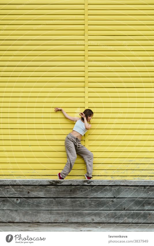 Junge erwachsene Frau in weißem Top und grauer Hose tanzt vor leuchtend gelber Wand Tänzer Choreograph hiphop im Freien Mädchen stylisch urban Bewegung Sport