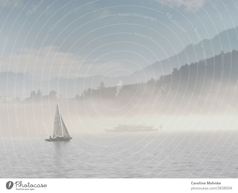 Eine seltene Nebelstimmung auf dem Vierwaldstättersee: Ein Segelschiff im Vordergrund, im Hintergrund eine Nebeldecke auf dem See. Darin ein weiteres Schiff zu erkennen und im Hintergrund die Alpen.
