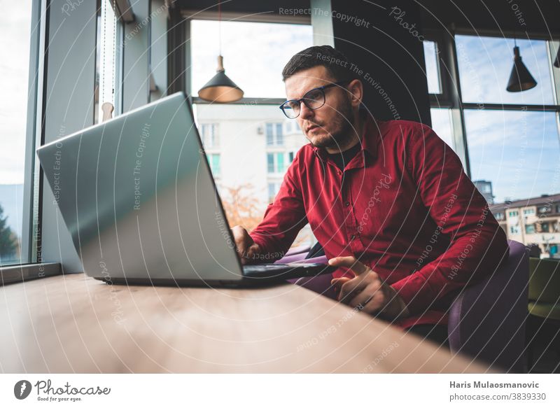 Freischaffender Mann im roten Hemd mit Brille, der am Laptop im Café arbeitet, Fernarbeit Business Geschäftsmann lässig Mitteilung Firmeninhaber Computer