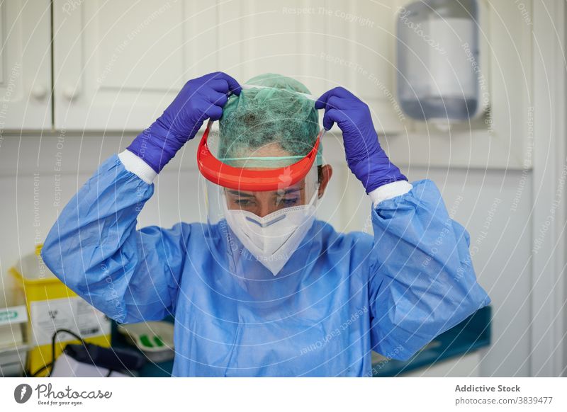 Anonymer Sanitäter in Uniform beim Anlegen des Gesichtsschutzes in der Klinik angezogen Schutzschild medizinisch steril Mundschutz Arbeitsplatz professionell