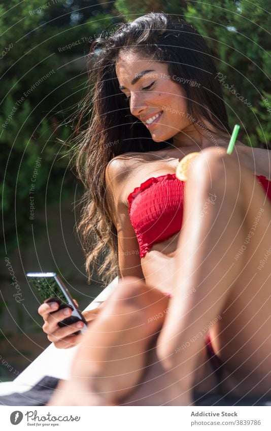 Sorglose Frau im Bikini entspannt am Pool Sonnenbad Bräune Beckenrand Liegestuhl Sommer Urlaub Cocktail sich[Akk] entspannen Smartphone frisch Saft Browsen