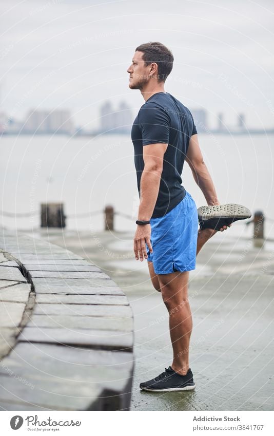 Männlicher Läufer streckt die Beine beim Training Aufwärmen Großstadt Mann Dehnung Stauanlage passen Sportler nass Straße männlich Vorwärtsbeuge Übung Wellness