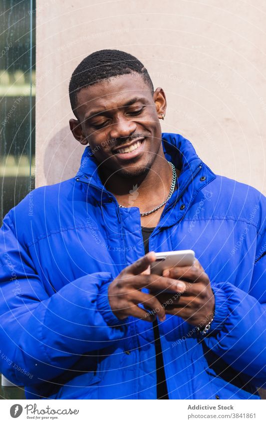 Fröhlich stilvollen schwarzen Mann Chatten auf sozialen Medien auf Handy Textnachricht Smartphone soziale Netzwerke Nachricht Talkrunde benutzend heiter
