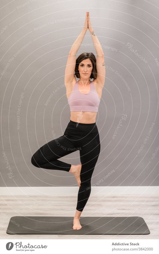 Schlanke Frau in Baum-Pose auf Yoga-Matte vrksasana Baumhaltung Gleichgewicht Barfuß Unterlage Seele Achtsamkeit Stressabbau Sportkleidung Inhalt schlanke