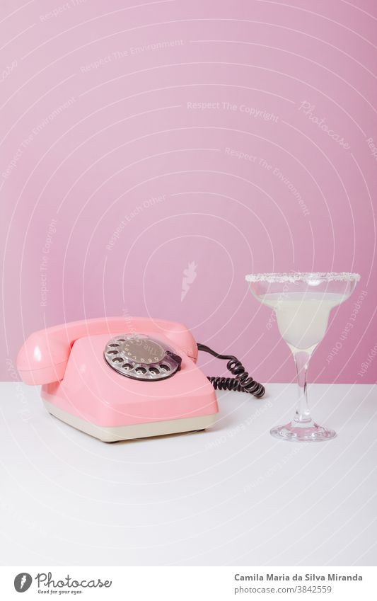 Vintage-Rosentelefon mit einem Getränk daneben. 60's 60s inserieren Hintergrund Anruf Farbe Textfreiraum Fünfziger für Text Spaß flippig Gute Neuigkeiten
